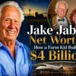 Jake Jabs net worth 2026 - Founder of American Furniture Warehouse smiling in blue shirt with private jet and city background