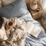 Person relaxing in bed during a calm lazy Sunday morning routine with tea and a book