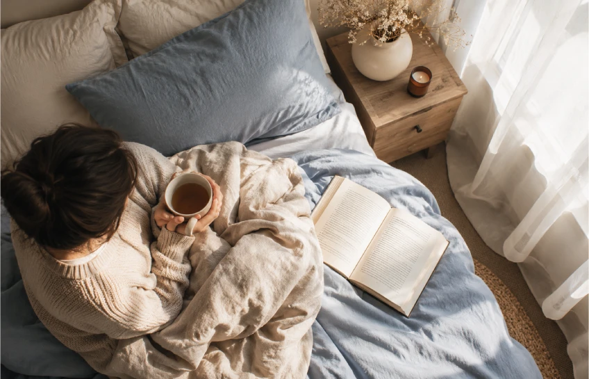 Person relaxing in bed during a calm lazy Sunday morning routine with tea and a book